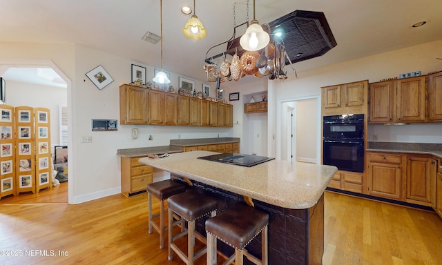 kitchen with arched walkways, a center island, brown cabinets, light wood-style flooring, and black appliances