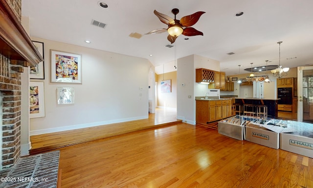 unfurnished living room featuring light wood-style floors, visible vents, a sink, and ceiling fan with notable chandelier