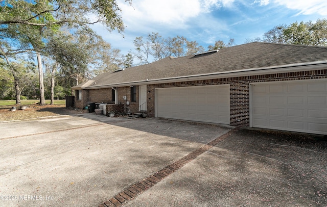 view of front of house with driveway, a shingled roof, an attached garage, and brick siding