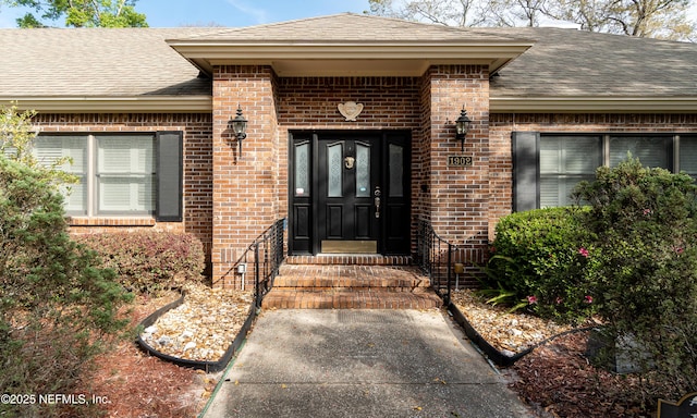 doorway to property featuring brick siding and roof with shingles