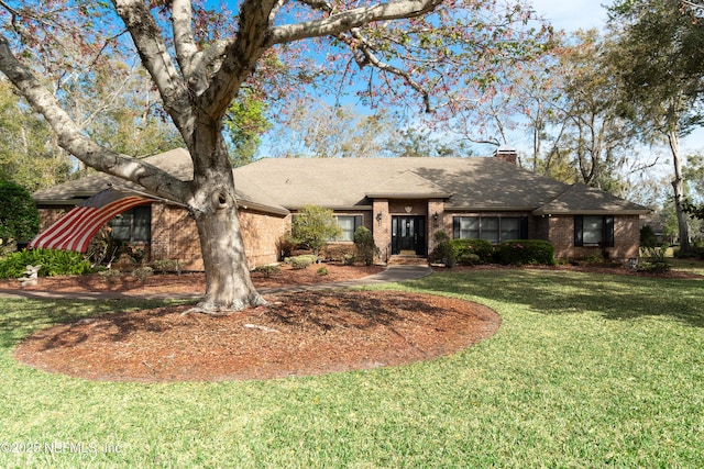 ranch-style house featuring a front lawn, a chimney, a shingled roof, and brick siding