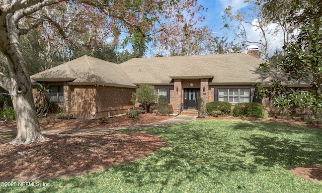 view of front of property with roof with shingles, brick siding, a chimney, and a front yard