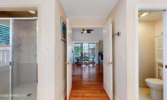 full bath featuring toilet, a stall shower, ceiling fan, wood finished floors, and wallpapered walls