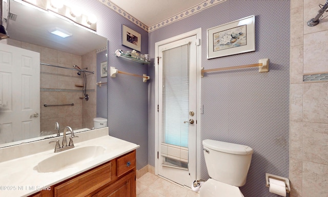 bathroom with toilet, vanity, tile patterned flooring, tiled shower, and wallpapered walls