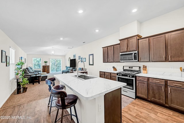 kitchen featuring light wood finished floors, a center island with sink, appliances with stainless steel finishes, open floor plan, and a sink