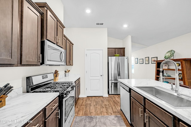 kitchen featuring dark brown cabinetry, a sink, light countertops, appliances with stainless steel finishes, and light wood-type flooring