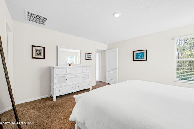 bedroom with a textured ceiling, dark colored carpet, visible vents, and baseboards