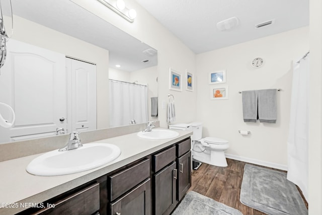 bathroom featuring toilet, visible vents, a sink, and wood finished floors