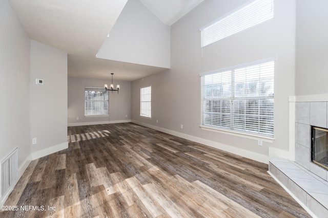 unfurnished living room with wood finished floors, baseboards, a tiled fireplace, and an inviting chandelier