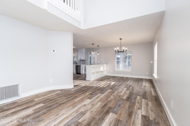 unfurnished living room with baseboards, visible vents, wood finished floors, an inviting chandelier, and a sink