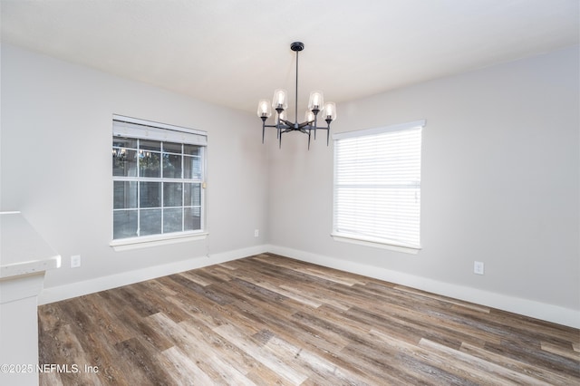 spare room with baseboards, a notable chandelier, and wood finished floors