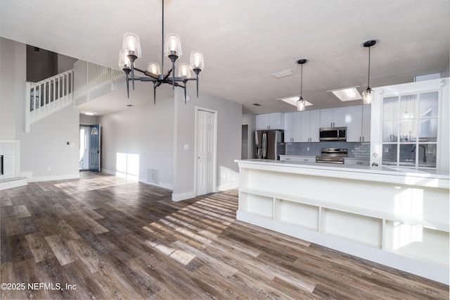 kitchen featuring a fireplace, dark wood finished floors, decorative backsplash, appliances with stainless steel finishes, and a textured ceiling