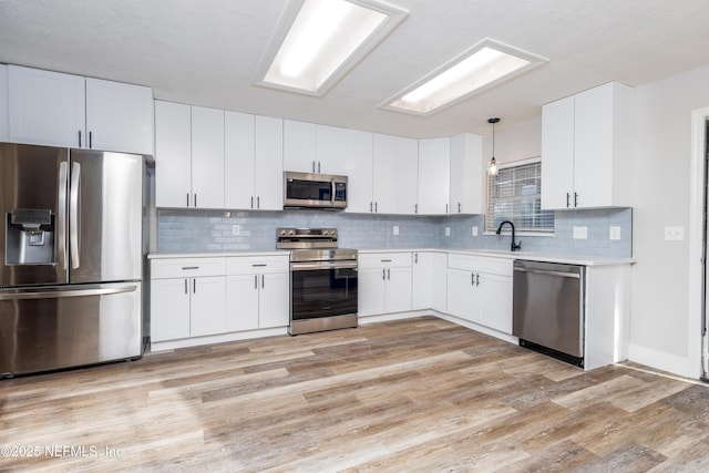 kitchen with light wood finished floors, tasteful backsplash, white cabinets, appliances with stainless steel finishes, and light countertops