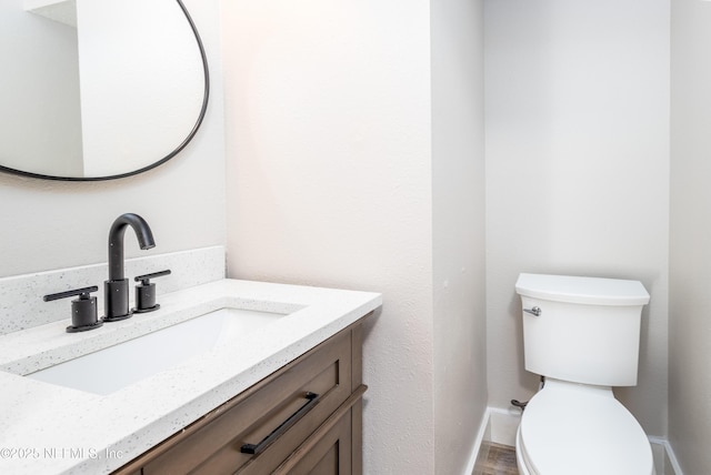 half bathroom featuring vanity, toilet, and baseboards