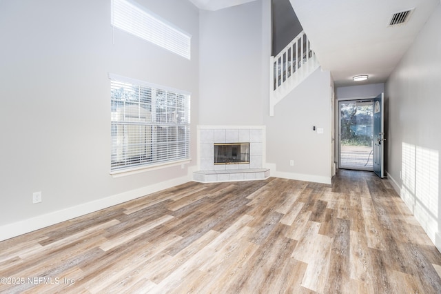 unfurnished living room with wood finished floors, a tile fireplace, visible vents, and baseboards