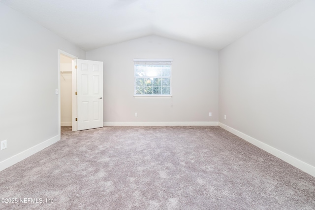 unfurnished bedroom featuring a spacious closet, baseboards, vaulted ceiling, and carpet flooring