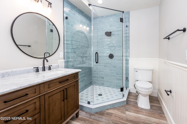 bathroom featuring wainscoting, toilet, wood finished floors, vanity, and a shower stall