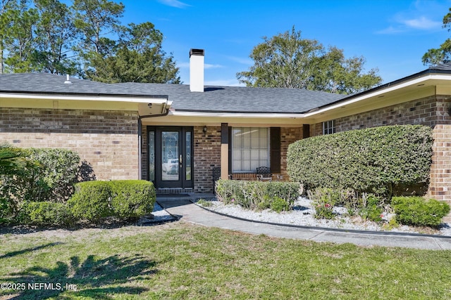 doorway to property featuring a lawn, brick siding, roof with shingles, and a chimney