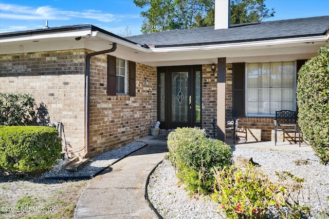 entrance to property featuring brick siding and a shingled roof