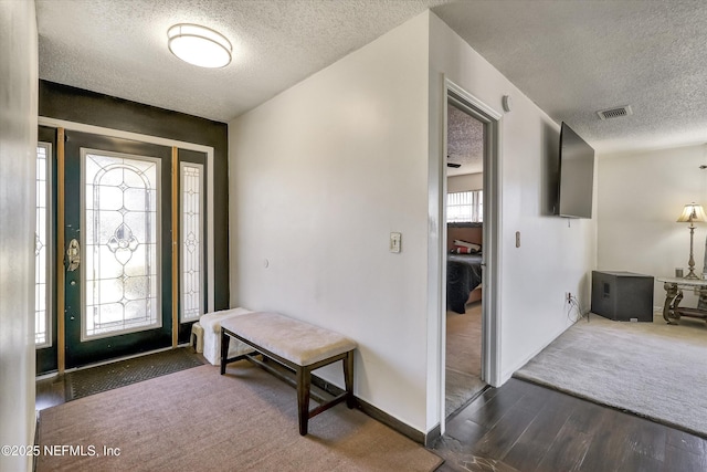 entryway with dark wood finished floors, baseboards, dark colored carpet, and a textured ceiling