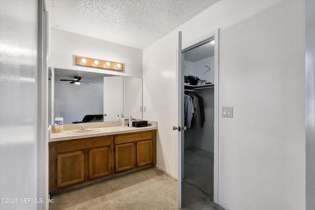 full bath with a spacious closet, double vanity, a textured ceiling, a ceiling fan, and a sink