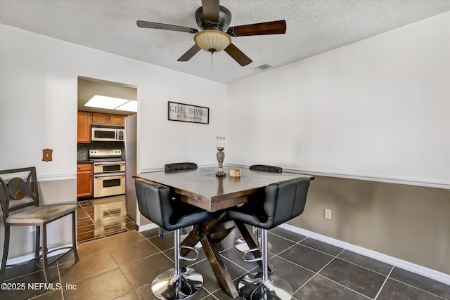 dining area featuring dark tile patterned floors, visible vents, a textured ceiling, and baseboards