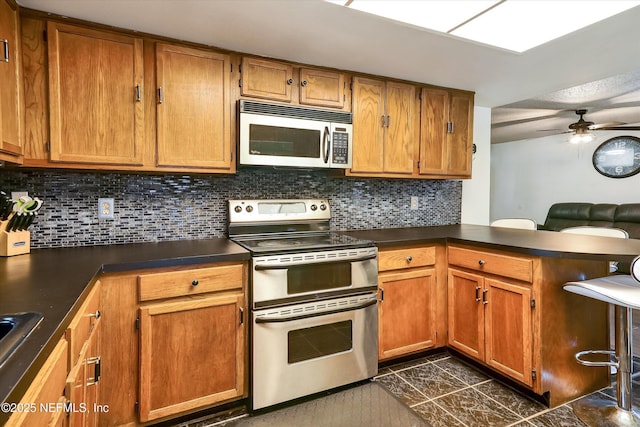 kitchen with dark countertops, a peninsula, tasteful backsplash, and appliances with stainless steel finishes