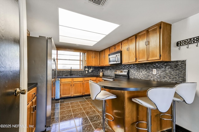 kitchen featuring visible vents, a sink, backsplash, stainless steel appliances, and a peninsula