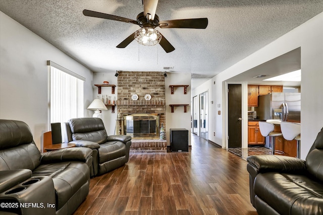 living room with visible vents, a ceiling fan, a textured ceiling, dark wood-style floors, and a brick fireplace