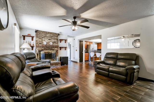 living room featuring a brick fireplace, a textured ceiling, ceiling fan, and wood finished floors