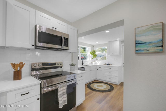 kitchen with light wood finished floors, backsplash, stainless steel appliances, white cabinetry, and a sink