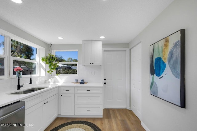 kitchen with light countertops, white cabinets, a sink, light wood-type flooring, and dishwasher