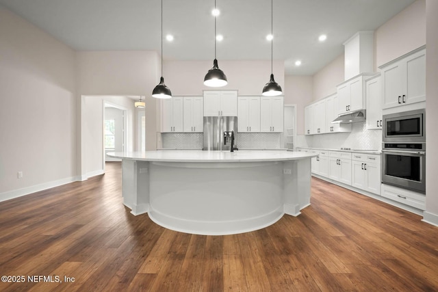 kitchen featuring dark wood finished floors, appliances with stainless steel finishes, light countertops, under cabinet range hood, and backsplash