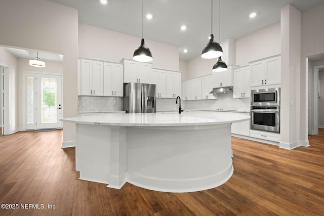 kitchen with dark wood-style flooring, a towering ceiling, appliances with stainless steel finishes, white cabinets, and under cabinet range hood