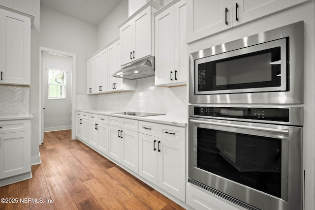 kitchen featuring stainless steel appliances, decorative backsplash, white cabinets, light wood-type flooring, and under cabinet range hood