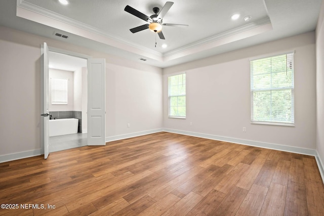 unfurnished bedroom with ornamental molding, a tray ceiling, wood-type flooring, and visible vents