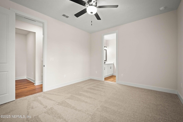 unfurnished bedroom featuring visible vents, baseboards, ceiling fan, ensuite bathroom, and carpet