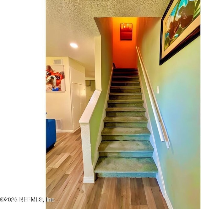 stairway featuring visible vents, baseboards, a textured ceiling, and wood finished floors