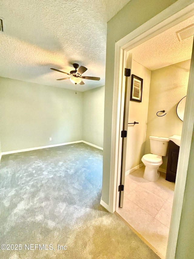 bathroom with ceiling fan, a textured ceiling, toilet, visible vents, and baseboards