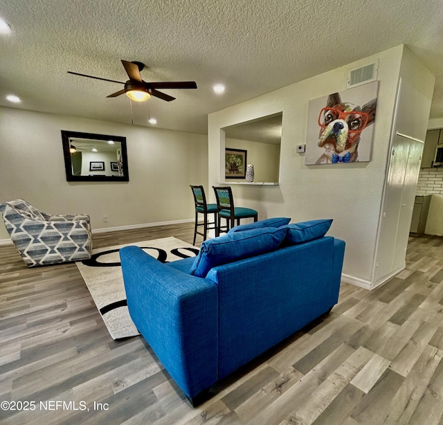 living area with baseboards, visible vents, ceiling fan, and wood finished floors