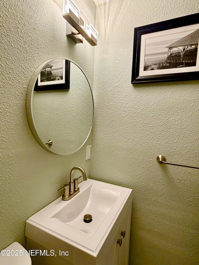 bathroom with a textured wall, vanity, and toilet