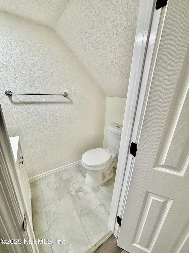 bathroom with baseboards, a textured wall, toilet, vaulted ceiling, and a textured ceiling