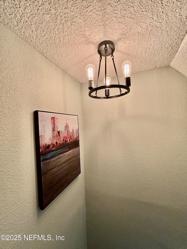 interior details with a textured ceiling, a textured wall, and an inviting chandelier