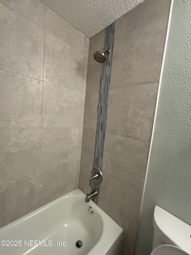 bathroom featuring a textured ceiling, tub / shower combination, and toilet