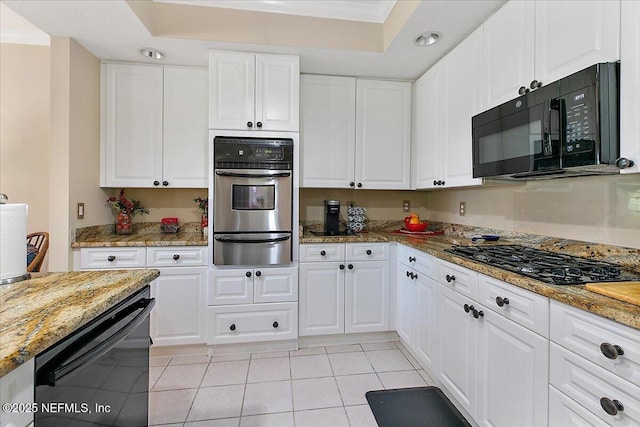 kitchen with light stone countertops, black appliances, white cabinets, and a warming drawer