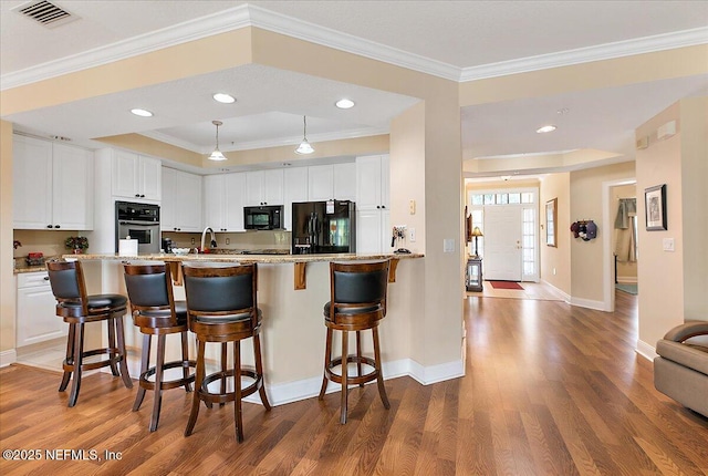 kitchen with black appliances, wood finished floors, visible vents, and white cabinets