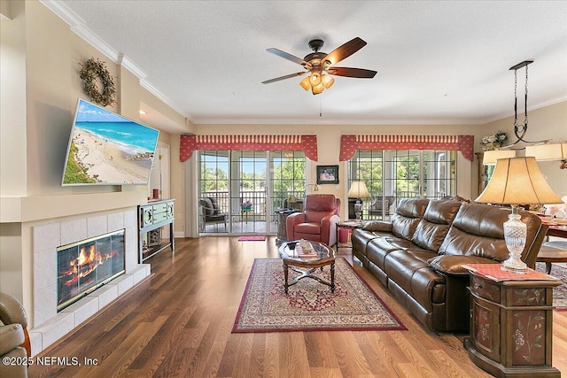 living area with ceiling fan, ornamental molding, a tiled fireplace, and wood finished floors