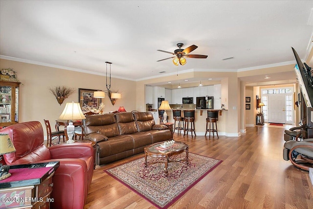 living room featuring light wood-style floors, ceiling fan, ornamental molding, and baseboards