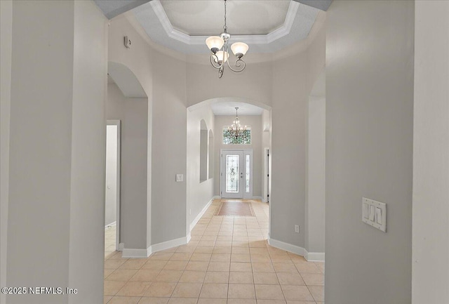 entrance foyer with arched walkways, light tile patterned flooring, a notable chandelier, baseboards, and a raised ceiling