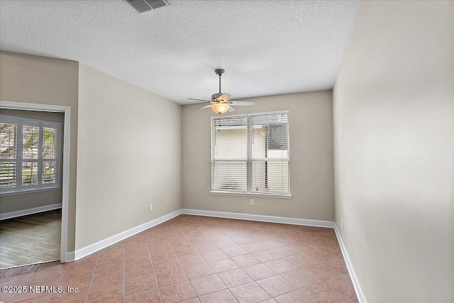 tiled empty room featuring ceiling fan, a textured ceiling, visible vents, and baseboards